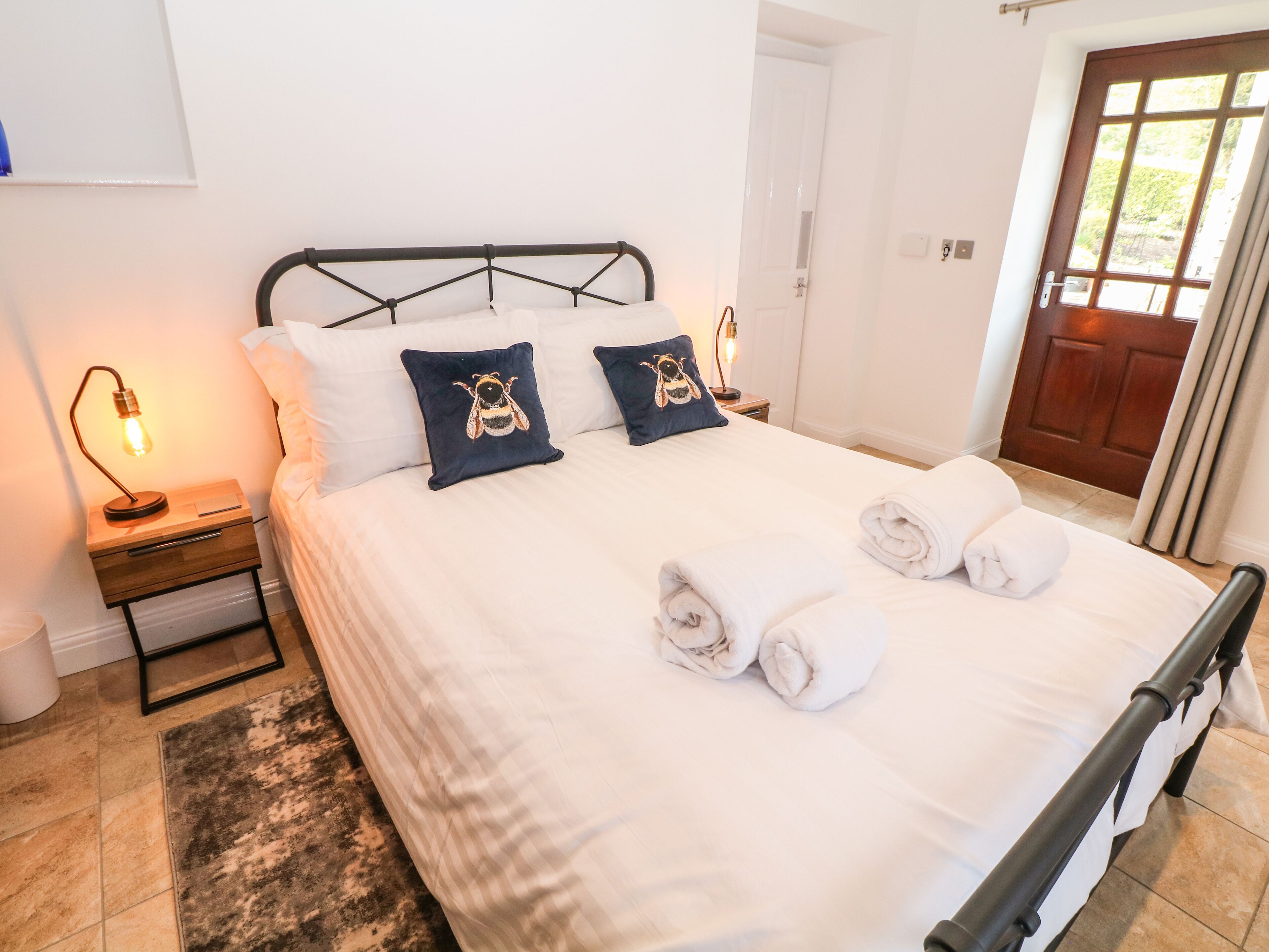 A neatly made bed with pillows, a bedside lamp, and a rolled towel on the floor.
