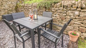 A stone wall, a wooden table with chairs, and a potted plant.