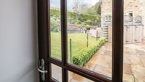 A view through a glass door into a garden with a stone pathway, a wooden fence, and a stone building.