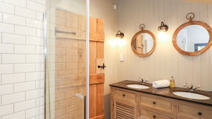 A bathroom with a glass shower enclosure, wooden vanity with two sinks, and wall-mounted lighting. - The Hare's Shack (Kendal)