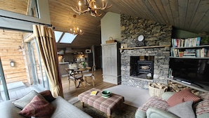 A cozy living room with a stone fireplace, wooden ceiling, and a dining area with a table and chairs. - The Hare's Shack (Kendal)