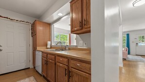 A kitchen with wooden cabinets, a dishwasher, and a window. - Cheerful 3-bedroom private home minutes to beach (Bay St. Louis)