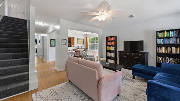 A living room with a staircase, a ceiling fan, a pink sofa, a blue sofa, and a bookshelf. - Cheerful 3-bedroom private home minutes to beach (Bay St. Louis)
