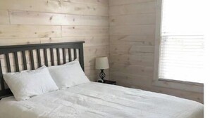 Un llit amb capçalera de fusta a una habitació amb parets de fusta i una finestra.