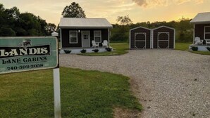 A property with a gravel driveway leading to a small house with a porch and two attached garages.