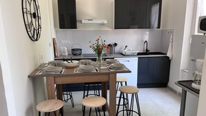 Uma cozinha moderna com área de jantar, apresentando uma mesa de madeira posta para quatro pessoas, banquetas, forno embutido e um armário preto grande acima do balcão.