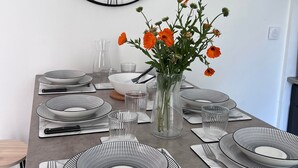 Uma mesa de jantar posta com pratos listrados em preto e branco, copos de vidro transparente e um vaso com flores laranjas.