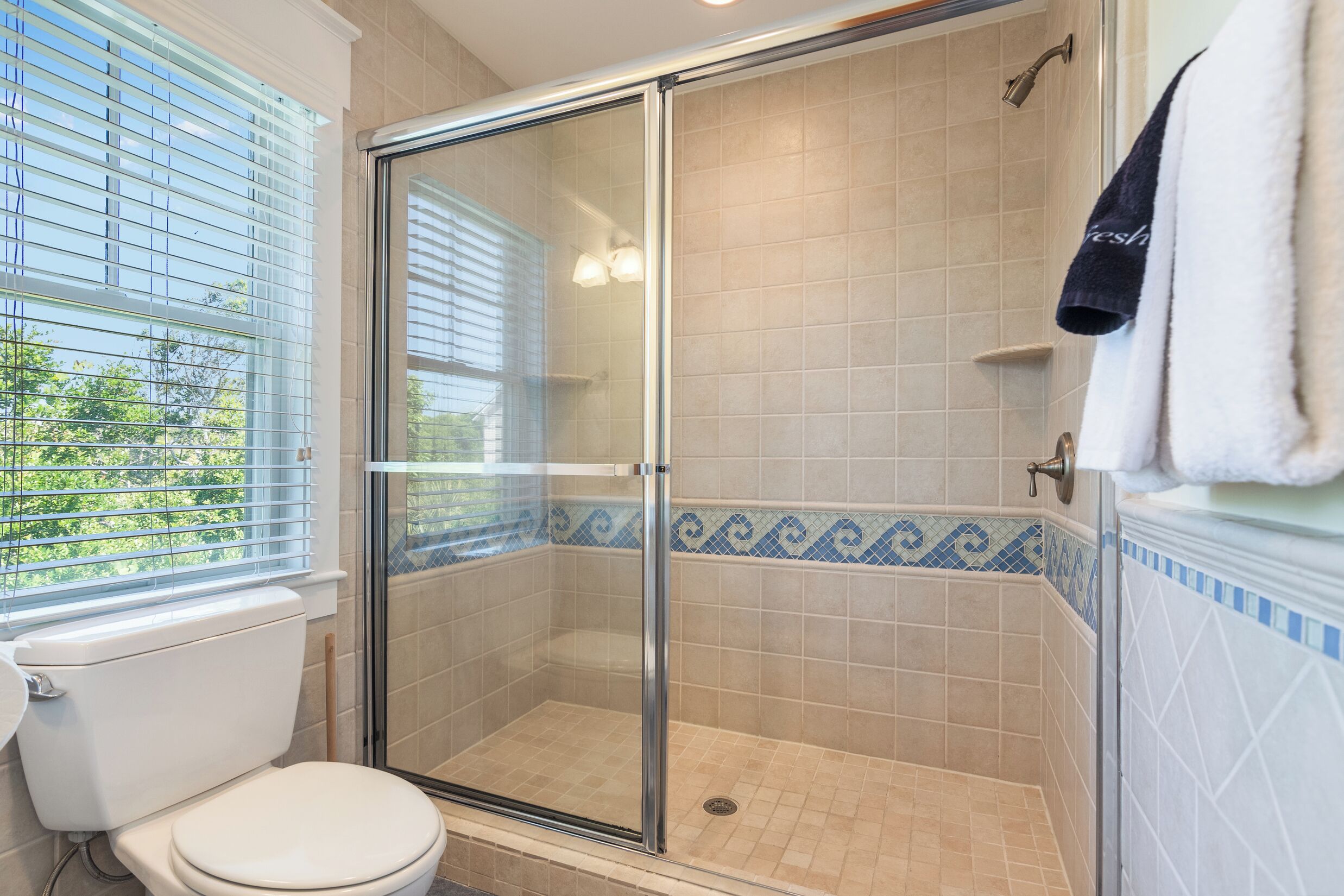 Un baño con ducha de vidrio, inodoro y ventana con persianas.