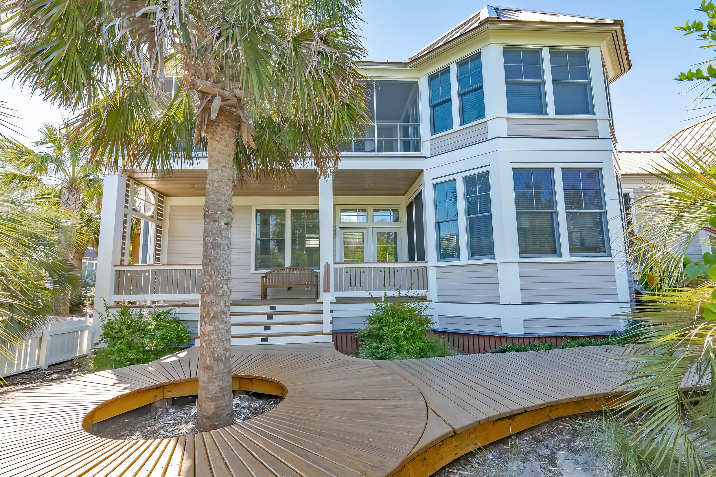 A two-story house with a balcony, a wooden deck, and a palm tree.