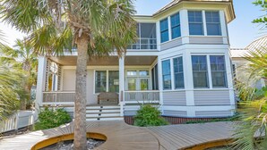 A two-story house with a balcony, a wooden deck, and a palm tree.