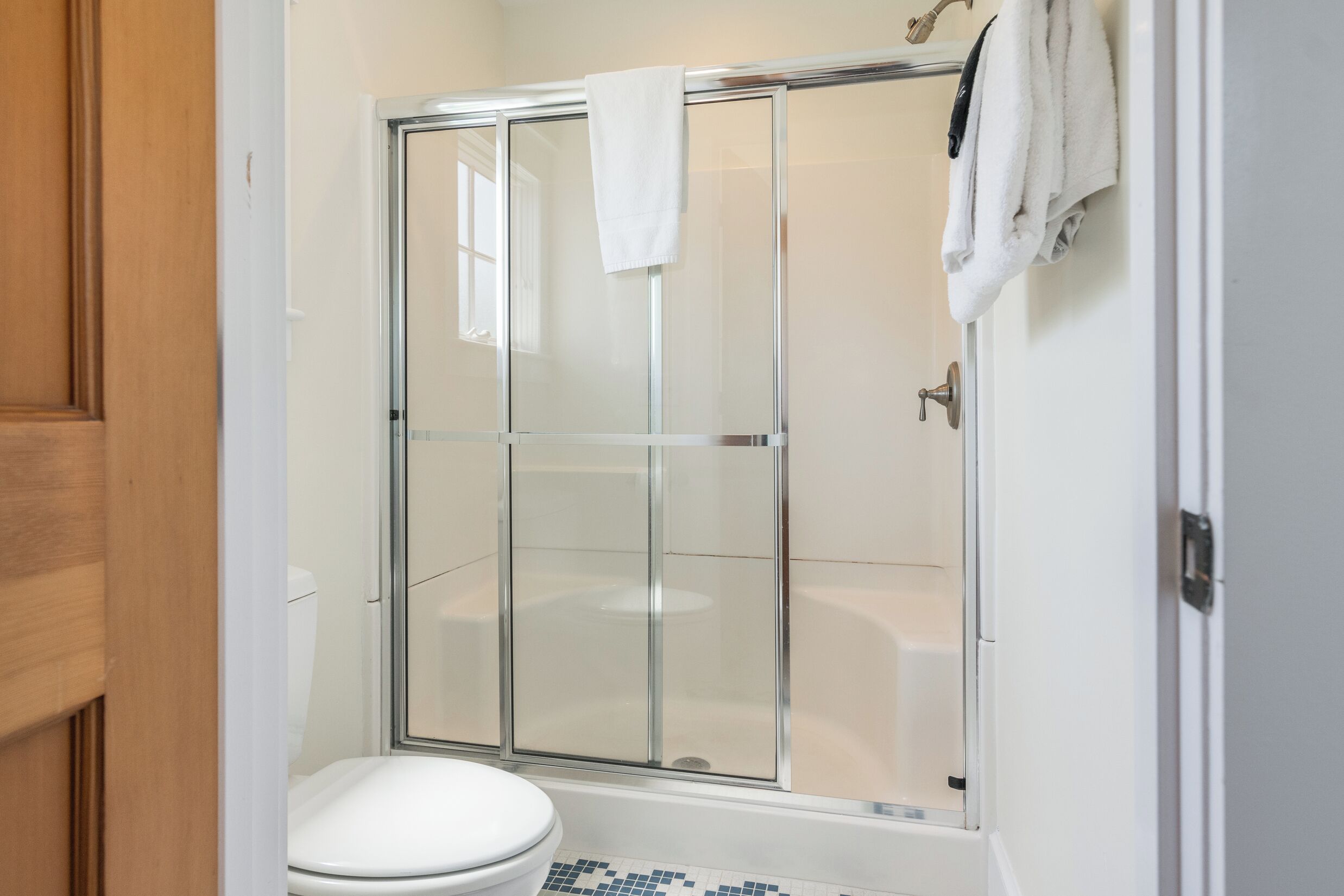 Un baño con cabina de ducha de vidrio, inodoro blanco y suelo de baldosas.