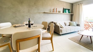 Uma sala de estar moderna com uma mesa de jantar redonda, sofá bege e uma cadeira de madeira.