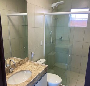 Um banheiro com chuveiro em box de vidro, pia com bancada de mármore e vaso sanitário.