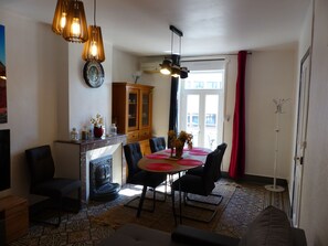 A dining area with a round table, chairs, a fireplace, and a kitchen area with cabinets and a clock.
