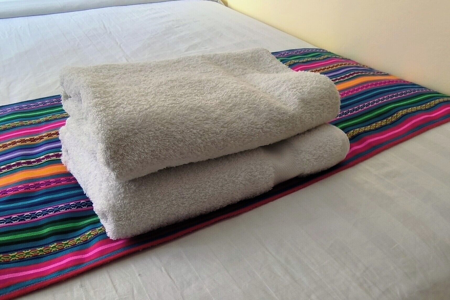 Una cama con un almohadón blanco y una manta a rayas de colores.