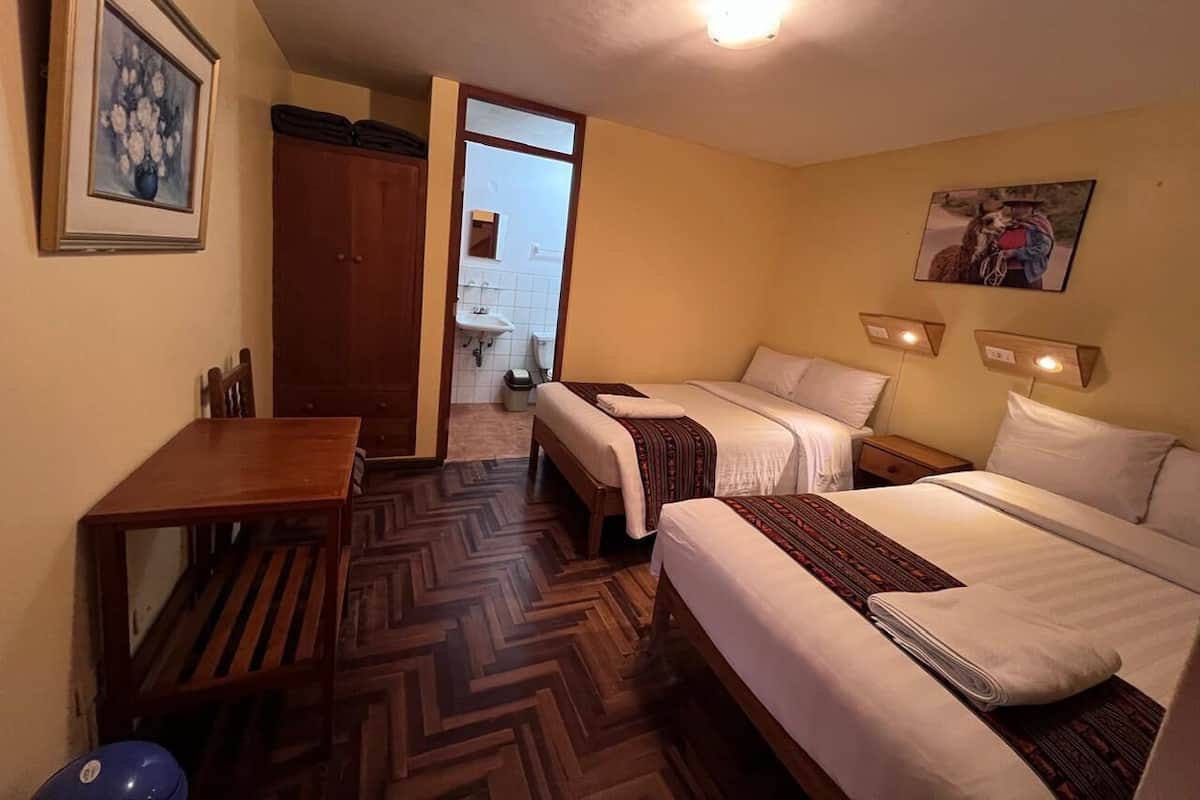 A hotel room with two beds, a wooden table, and a view of the bathroom.