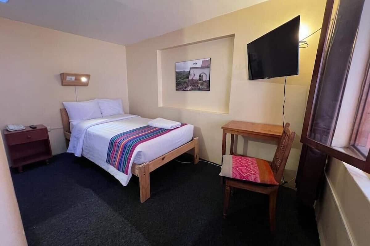 A hotel room with a bed, bedside table, chair, TV, and a framed picture on the wall.