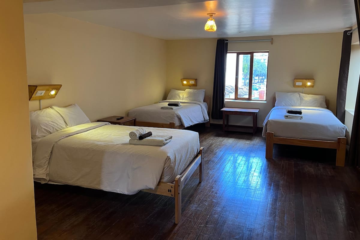 A hotel room with two single beds, a small table, a window with curtains, and a ceiling light.