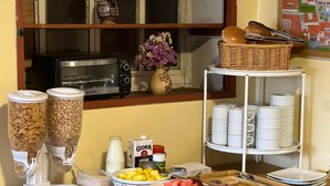 A breakfast buffet setup with cereal dispensers, milk, fruit, and a toaster oven. - Eco Inn (Cusco)