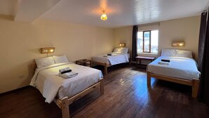 A room with three wooden beds, each with a headboard and bedside table. There is a window with curtains, and a small table between the beds. - Eco Inn (Cusco)