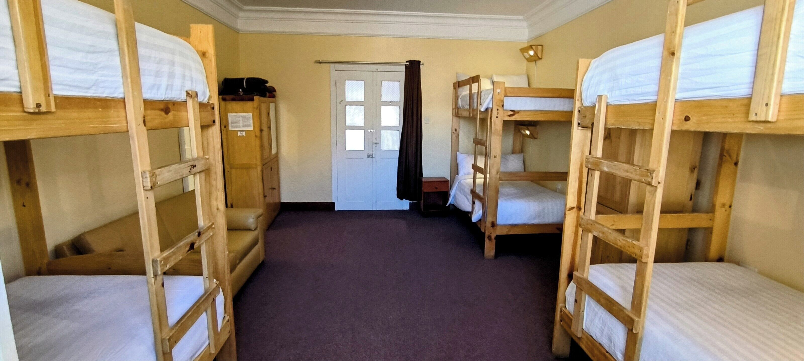 A room with bunk beds arranged in a row, a door with windows, and a carpeted floor.