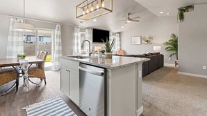 Una cocina moderna con una isla central, electrodomésticos de acero inoxidable y un comedor con mobiliario de mimbre.