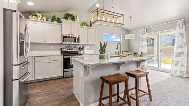 Cocina moderna con gabinetes blancos, electrodomésticos de acero inoxidable, una isla central con taburetes y una lámpara colgante.