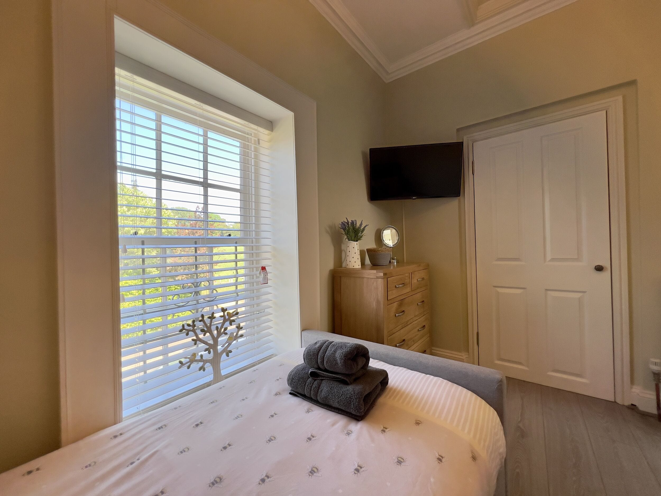 A bedroom with a bed, a dresser, a television, and a window with blinds.