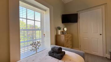A bedroom with a bed, a dresser, a television, and a window with blinds.