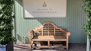 A wooden bench under a sign that reads "WELCOME TO SANDRINGHAM" with a crown symbol above the text. - May Bell Cottage (King's Lynn)