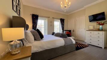 A bedroom with a bed, a dresser, a television, and a chandelier.
