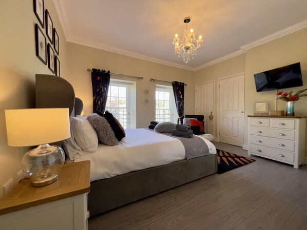 A bedroom with a bed, a dresser, a television, and a chandelier.