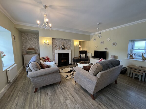 A living room with two grey sofas, a fireplace, a TV, and a chandelier. - May Bell Cottage (King's Lynn)