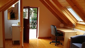 Un dormitorio acogedor en el ático con vigas de madera, tragaluces, un escritorio y una cama con una colcha de cuadros.