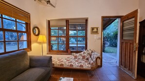 Una habitación acogedora con sofá, un ventanal con vistas al jardín, una lámpara y una puerta que da al exterior.