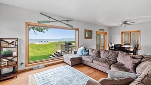 A spacious living room with a large window offering a view of the outdoors, a cozy sectional sofa, a dining area with a table and chairs, and a ceiling fan.