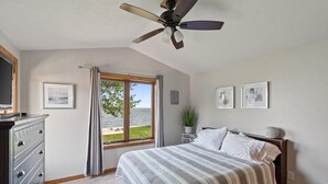A bedroom with a bed, a dresser, a ceiling fan, a window with curtains, and framed pictures on the wall.