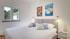 A bedroom with a large bed, two wall-mounted lights, and two paintings. - Cottage only 20 meters from the beach (Premantura)