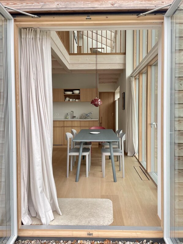A compact kitchen with wooden cabinets, a dining table with chairs, and a red pendant light.