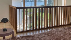 Una habitación con un ventanal grande que da a una masa de agua, baranda de madera y cama con manta.