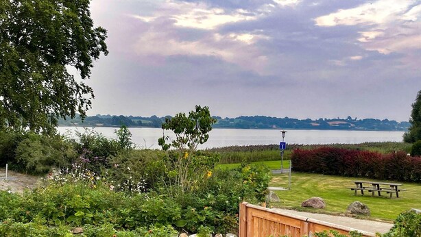 Un jardín junto al lago con una mesa de picnic, un cobertizo de madera y un farol.