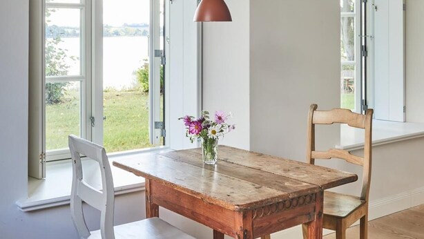 En matplats med ett träbord, två stolar, en hängande taklampa och stora fönster med öppna fönsterluckor.
