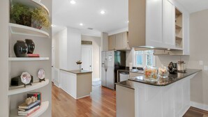 A modern kitchen with white cabinetry, a central island, and built-in shelves with decorative items. - 🐟350yds 2 Beach-Porch-Magnolia Cottage (Inlet Beach)