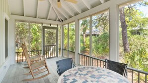 A covered patio with a ceiling fan, a rocking chair, a table with chairs, and large windows offering views of trees and a house. - 🐟350yds 2 Beach-Porch-Magnolia Cottage (Inlet Beach)