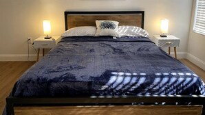 Une chambre à coucher avec une tête de lit en bois, une couvre-lit bleu foncé, deux tables de chevet avec des lampes et un tableau encadré au mur.