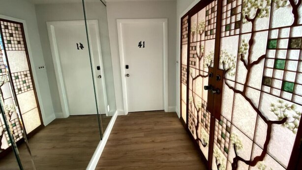 Un couloir doté d’un plancher en bois, de deux portes blanches portant les numéros 14 et 41, et d’une cloison décorative en verre ornée de motifs floraux.