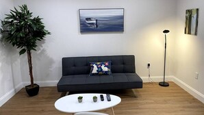 Un salon avec un canapé gris foncé, une table basse blanche, une plante en pot et un tableau représentant un bateau accroché au mur.