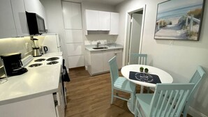 Une cuisine de taille réduite avec des meubles blancs, un coin repas comprenant une table ronde et quatre chaises, et un tableau accroché au mur.