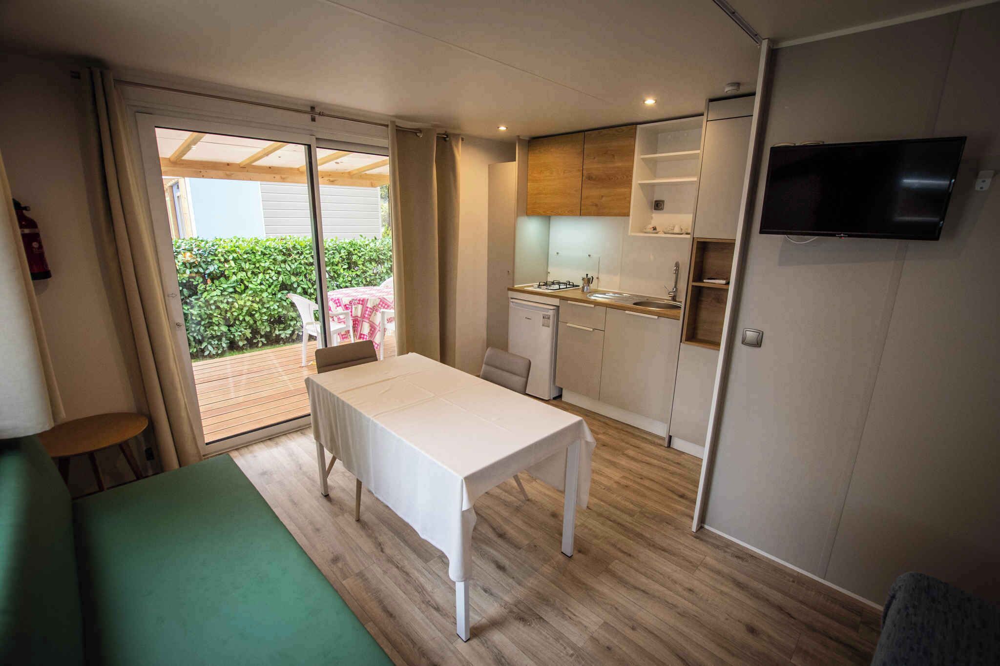 A compact kitchen with a dining table, a TV mounted on the wall, and a sliding glass door leading to an outdoor area.