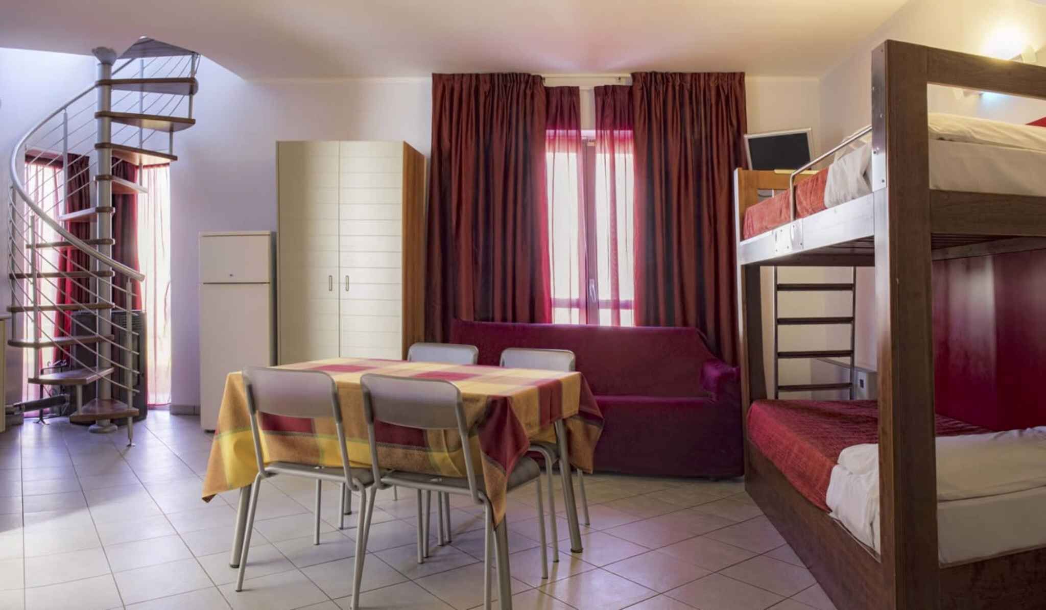 A room with a bunk bed, a desk with chairs, a sofa, a wardrobe, and a spiral staircase.